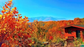 A cabin with a mountain backdrop, surrounded by autumn foliage. - Stunning Mtn View, True Log Cabin, Romance Getaway, Rare Find (Gatlinburg)