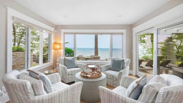 A spacious living area with large windows, a round coffee table, and striped armchairs. - Juniper Presents: Magnificent Lakefront Vacay Home on the Beach (Coloma)