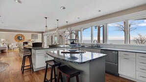 A modern kitchen with a large island, white cabinetry, and a view of the outdoors. - Juniper Presents: Magnificent Lakefront Vacay Home on the Beach (Coloma)
