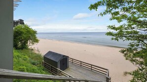A wooden deck leading to a beach with a small shed and a view of the ocean. - Juniper Presents: Magnificent Lakefront Vacay Home on the Beach (Coloma)