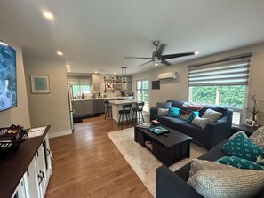 A modern living room with a dark sofa, a coffee table, and a kitchen in the background.
