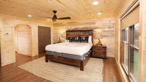A wooden cabin bedroom with a bed, a ceiling fan, a nightstand, and a window.