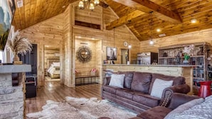 A rustic wooden interior with a leather sofa, a stone fireplace, and a dining area.