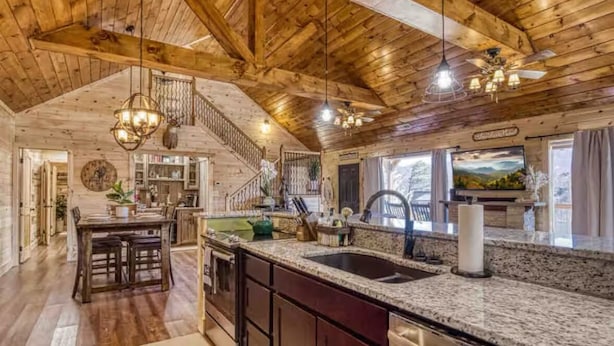 A rustic kitchen with wooden beams, granite countertops, and a large island with a sink.