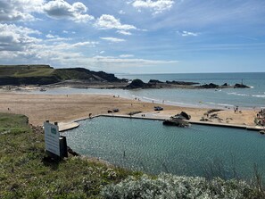 A coastal view with a swimming pool, beach, and rocky cliffs.