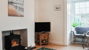 A living room with a fireplace, a television, a chair, and a window with a view of the outside. - 3 bedroom accommodation in Bude (Bude)