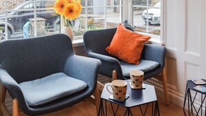 A room with two blue chairs, a small table with two coffee mugs, and a vase with yellow flowers. - 3 bedroom accommodation in Bude (Bude)