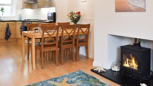 A cozy living room with a fireplace, wooden dining table, and chairs. - 3 bedroom accommodation in Bude (Bude)