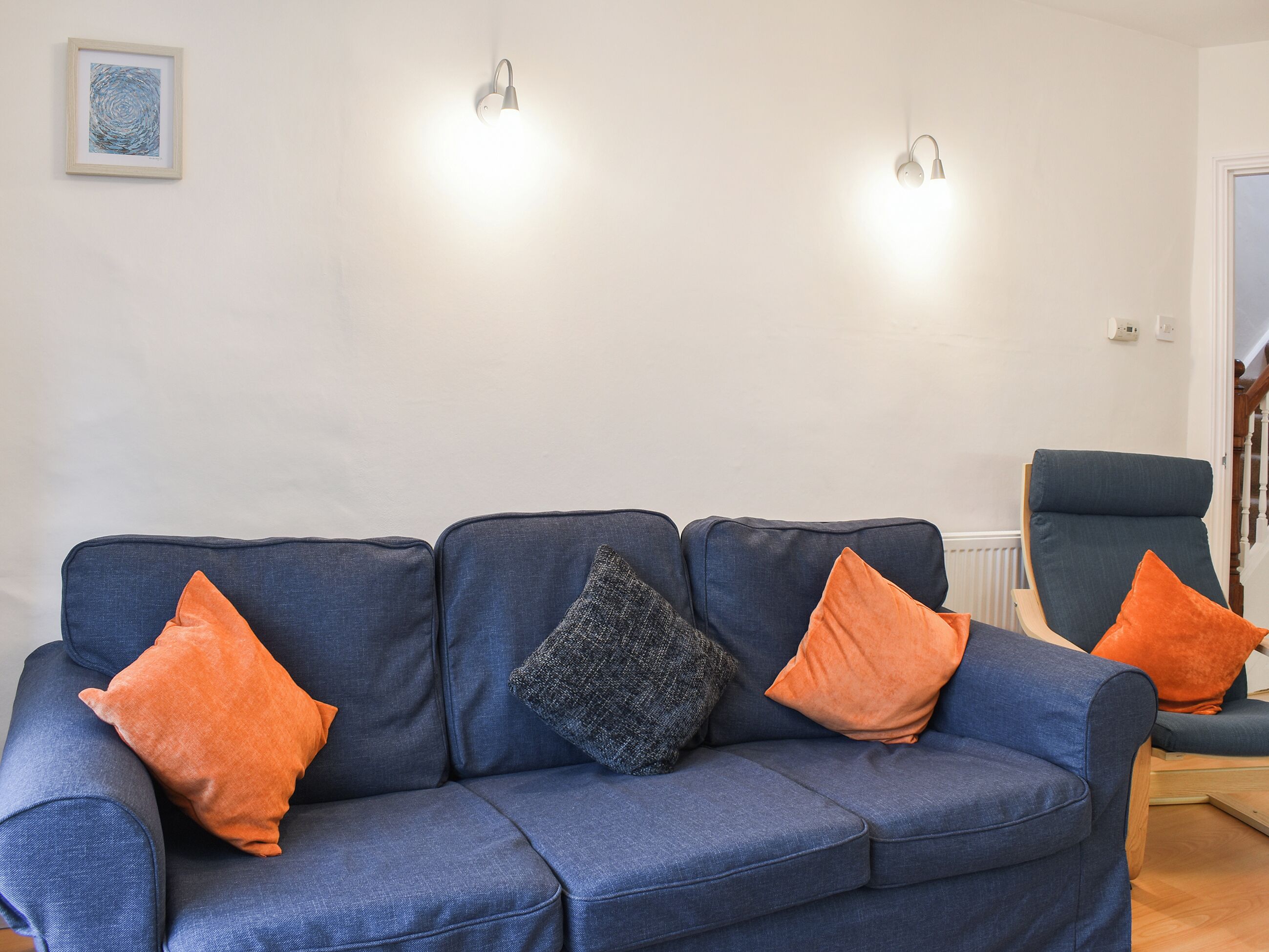 A blue sofa with three cushions, two wall-mounted lights, and a framed artwork on the wall.
