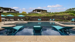 Ein Swimmingpool mit Liegestühlen und Sonnenschirmen, umgeben von einer Steinmauer und viel Grün.