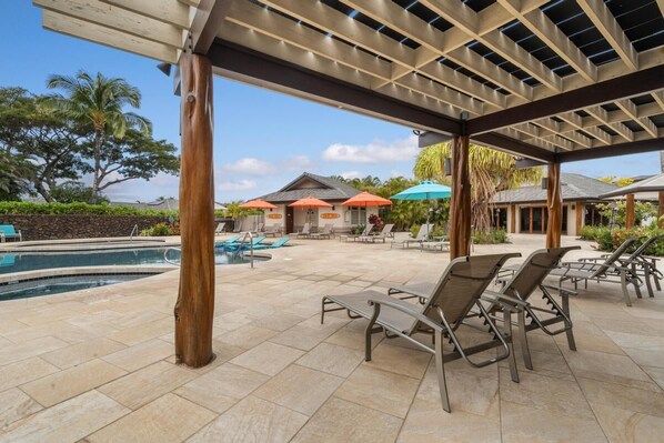 A covered outdoor area with a pool, lounge chairs, and umbrellas.