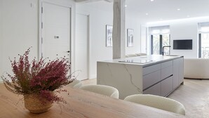 A modern kitchen with a marble island, white cabinetry, and a built-in TV.