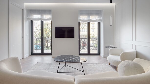 A modern living room with a round black table, white sofas, and a flat-screen TV mounted on the wall.