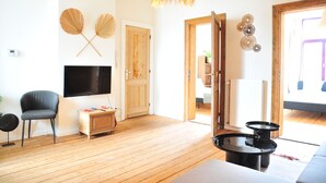 A living room with wooden flooring, a flat-screen TV, a grey chair, a wooden cabinet, and a black coffee table. - Boho Apartments 2 Bedrooms (Antwerp)