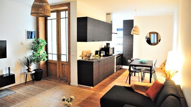 A modern kitchen with dark cabinets, a dining area with a table and chairs, and a cozy living space with a sofa. - Boho Apartments 2 Bedrooms (Antwerp)