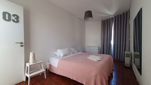 A hotel room with a bed, a bedside table, a lamp, a window with curtains, and a door with a number. - The Story Guest House  (Faro)