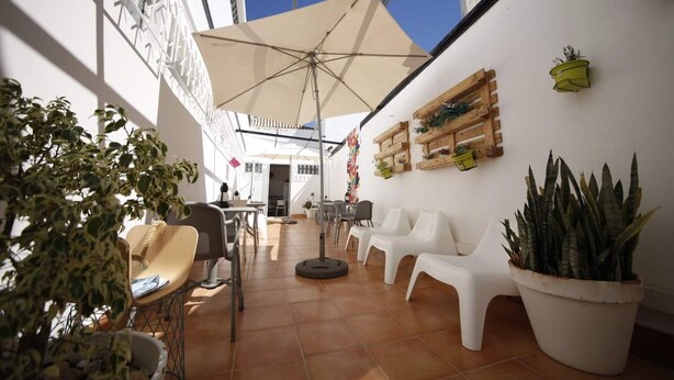 A sunlit outdoor patio with white plastic chairs, a large umbrella, and potted plants. - The Story Guest House  (Faro)