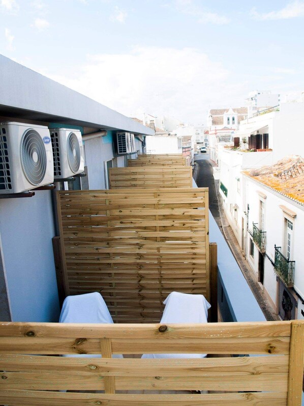 A narrow outdoor corridor with a wooden bench and two air conditioning units on the left.