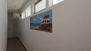 A hallway with a painting of a van by the sea, a door, and a ceiling light fixture. - The Story Guest House  (Faro)