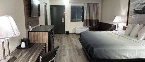 A hotel room with a bed, desk, chair, TV, and a window with curtains.