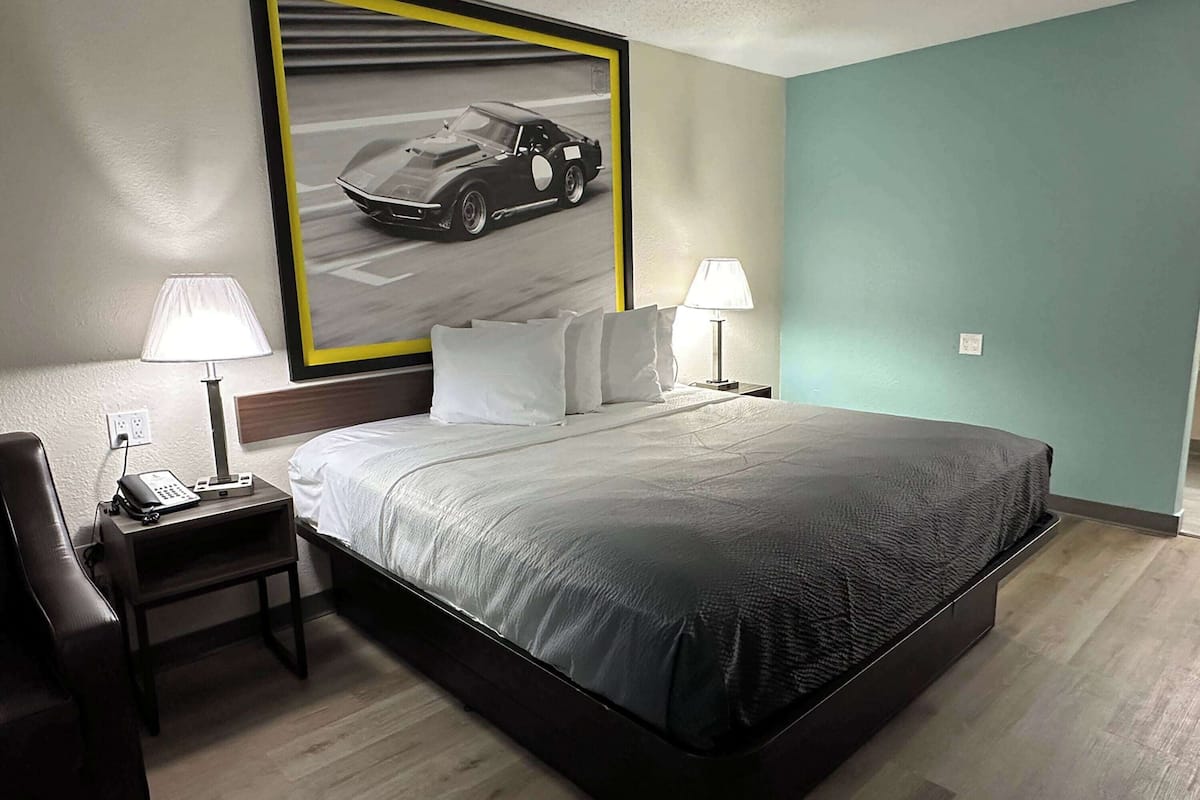 Ett hotellrum med en stor säng, två sängbord med lampor, en telefon på det vänstra bordet och en inramad bild av en bil på väggen.