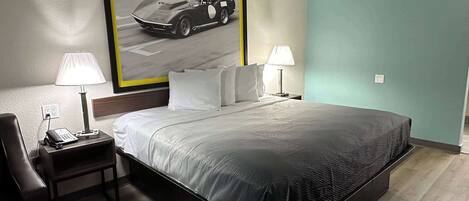 Una habitación de hotel con una cama grande, dos mesitas de noche con lámparas, un teléfono en la mesa de la izquierda y un cuadro con una foto de un coche en la pared.