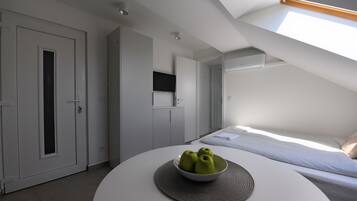 Un dormitorio moderno con tragaluces, una mesa redonda con un cuenco de manzanas y una cama con colcha estampada.
