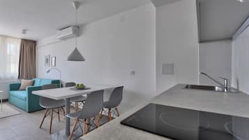 Una cocina moderna con estufa integrada, un comedor con mesa blanca y sillas grises, y un sofá azul aguamarina en la sala de estar.