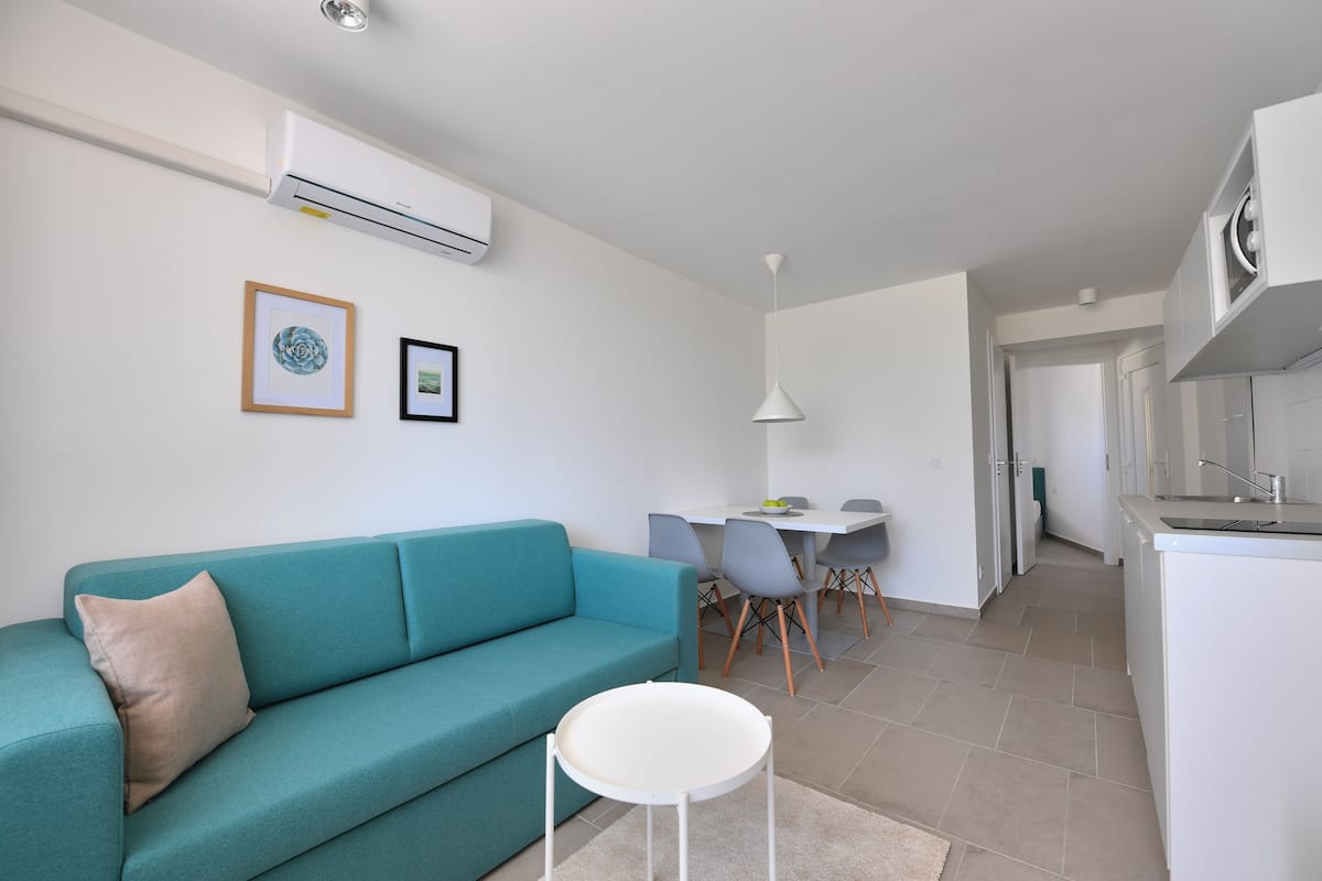 Uma sala de estar moderna com um sofá verde-água, uma mesinha branca e uma área de jantar com cadeiras e uma mesa.