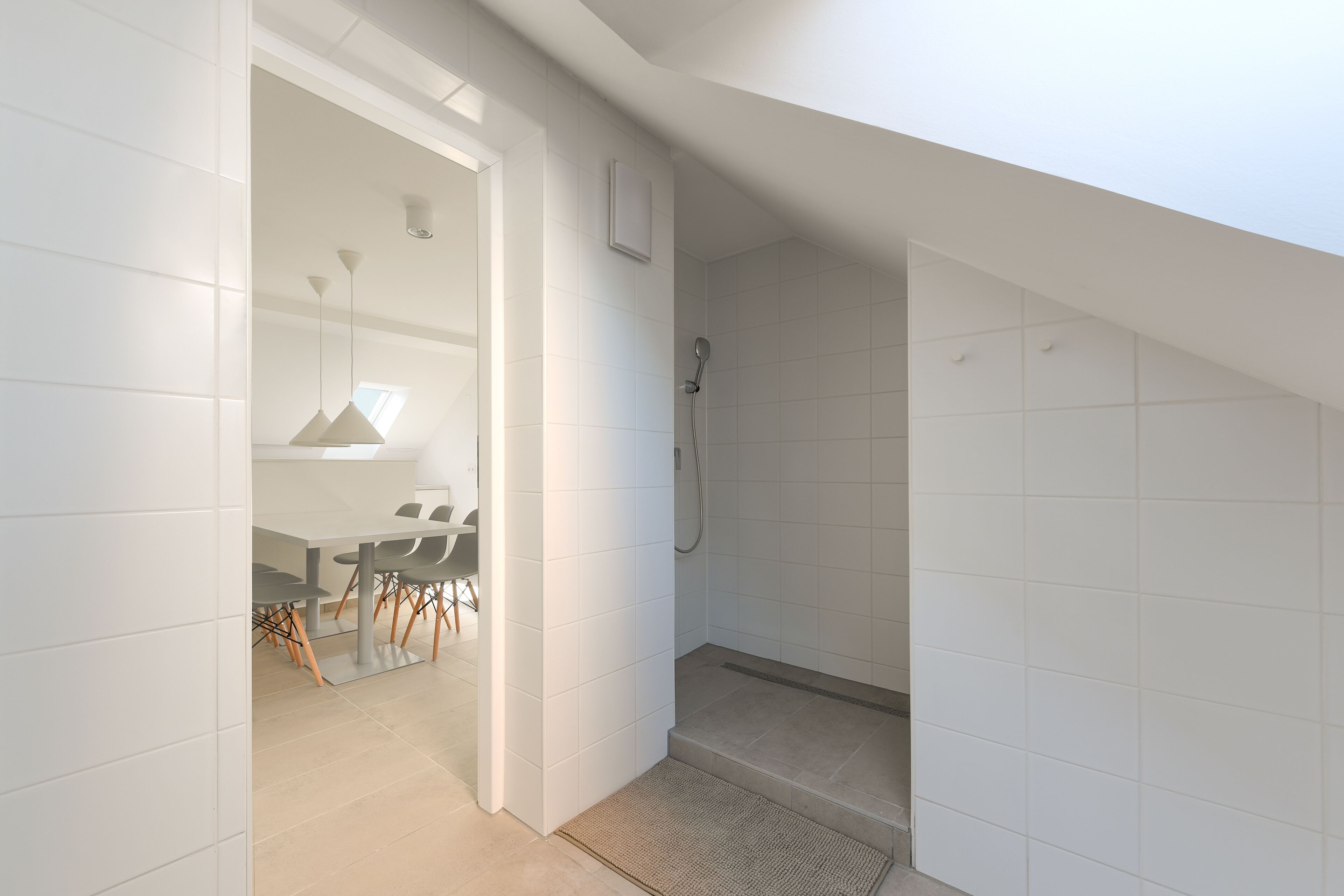 A modern bathroom with white tiles, a shower, and a small seating area with a table and chairs.
