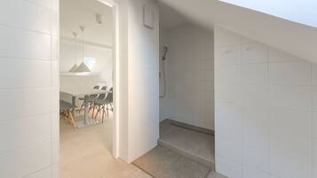 A modern bathroom with white tiles, a shower, and a small seating area with a table and chairs.
