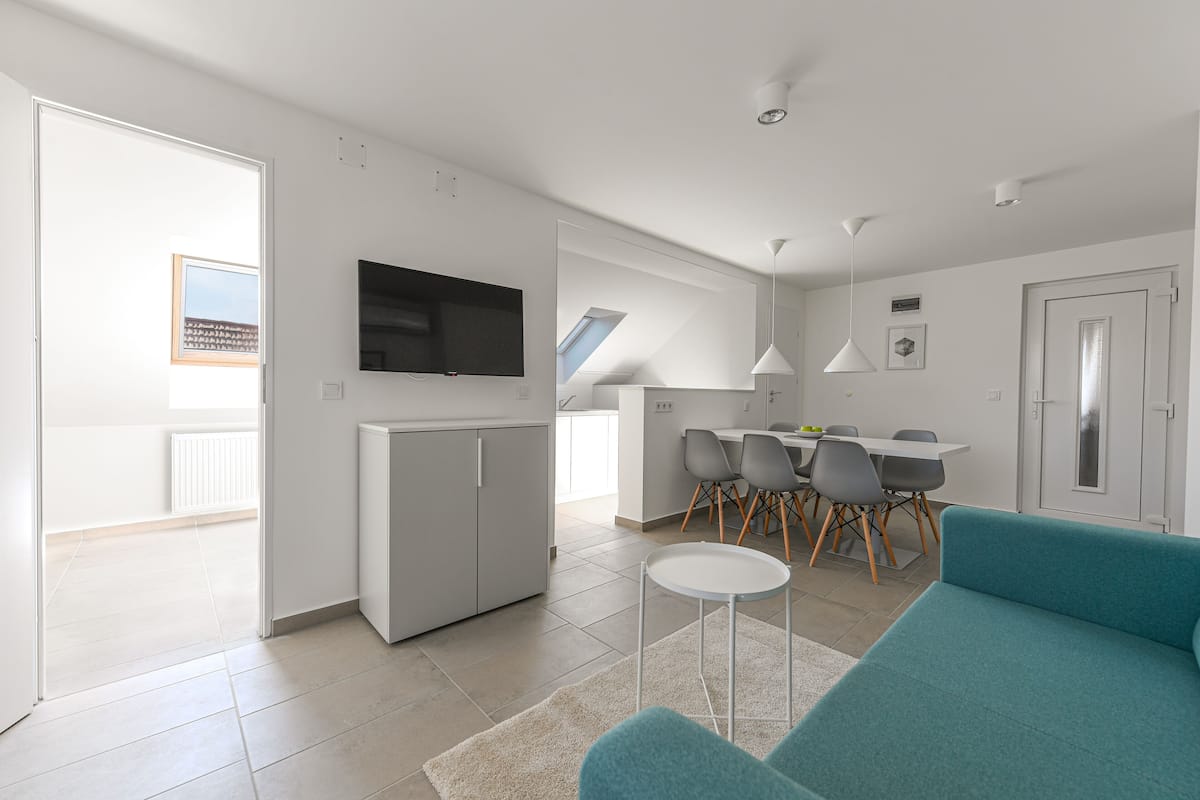 Uma sala de estar moderna com um sofá azul-turquesa, uma TV de tela plana e uma área de jantar com mesa e cadeiras.