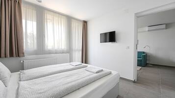 Quarto de hotel moderno com uma cama grande, uma TV de tela plana e vista para o exterior através de cortinas translúcidas.