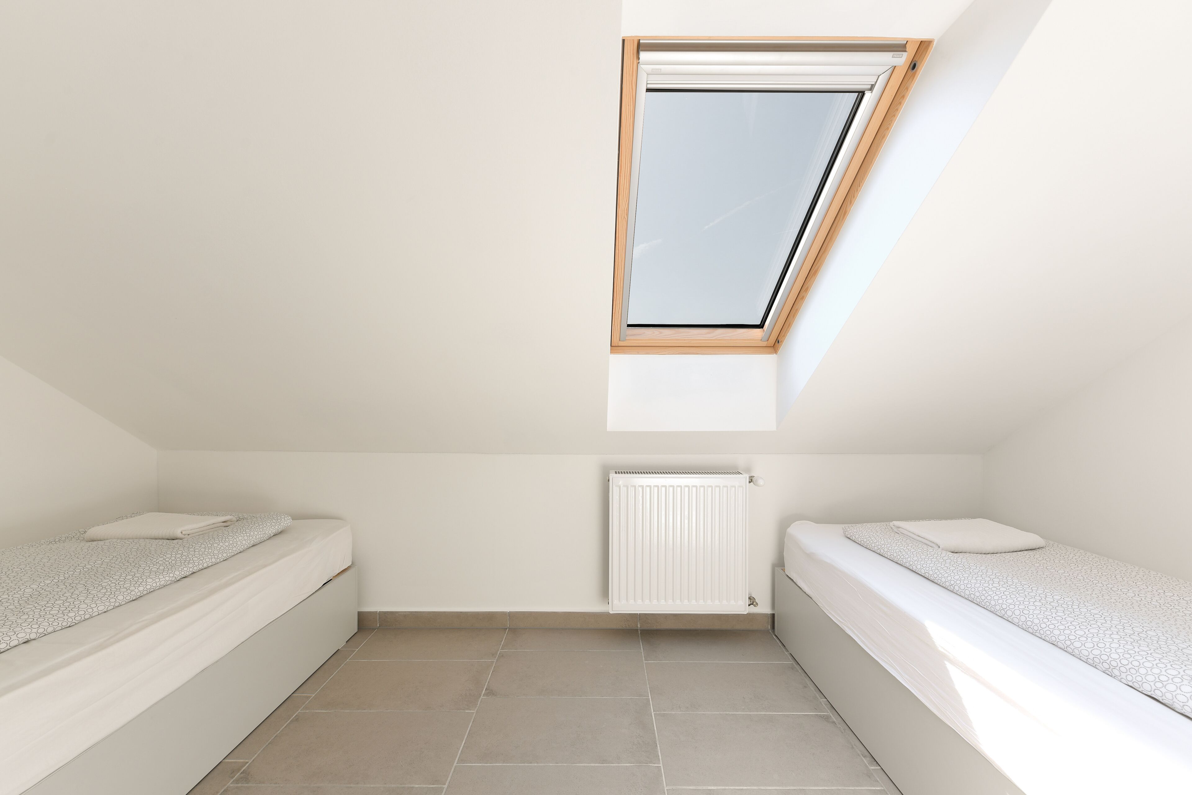 A small, clean room with two beds, a skylight, and a radiator.