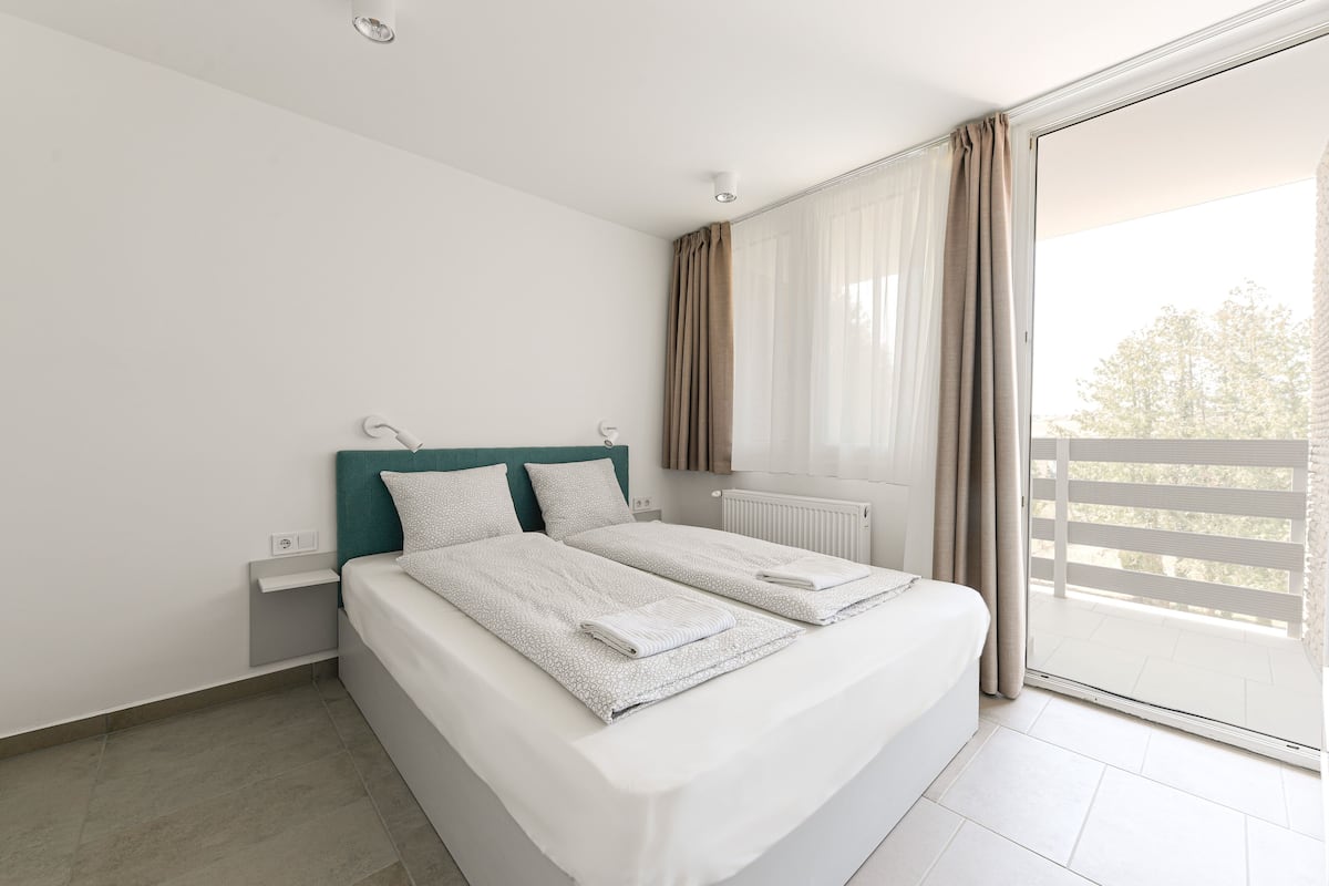 Quarto moderno com uma cama grande, uma janela com cortinas e vista para o exterior.
