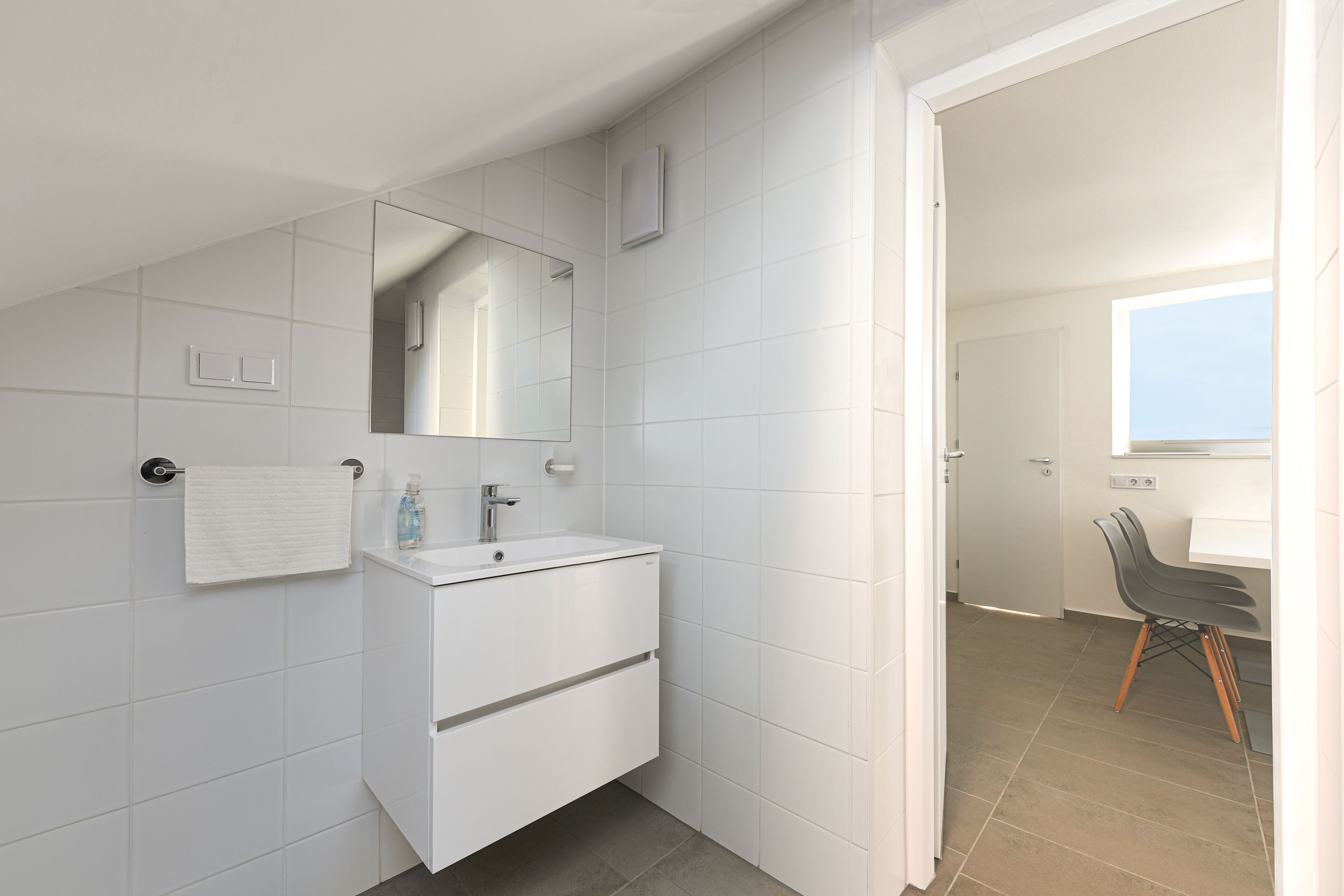 Een moderne badkamer met een wit wastafelmeubel, een spiegel en een handdoek aan de muur.