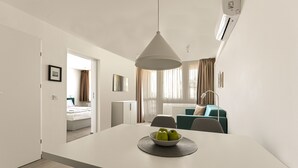 A modern, well-lit room with a dining table, a bowl of fruit, and a view of a bedroom and living area through an open door. - Villa Oliver Hévíz 1 (Hévíz)