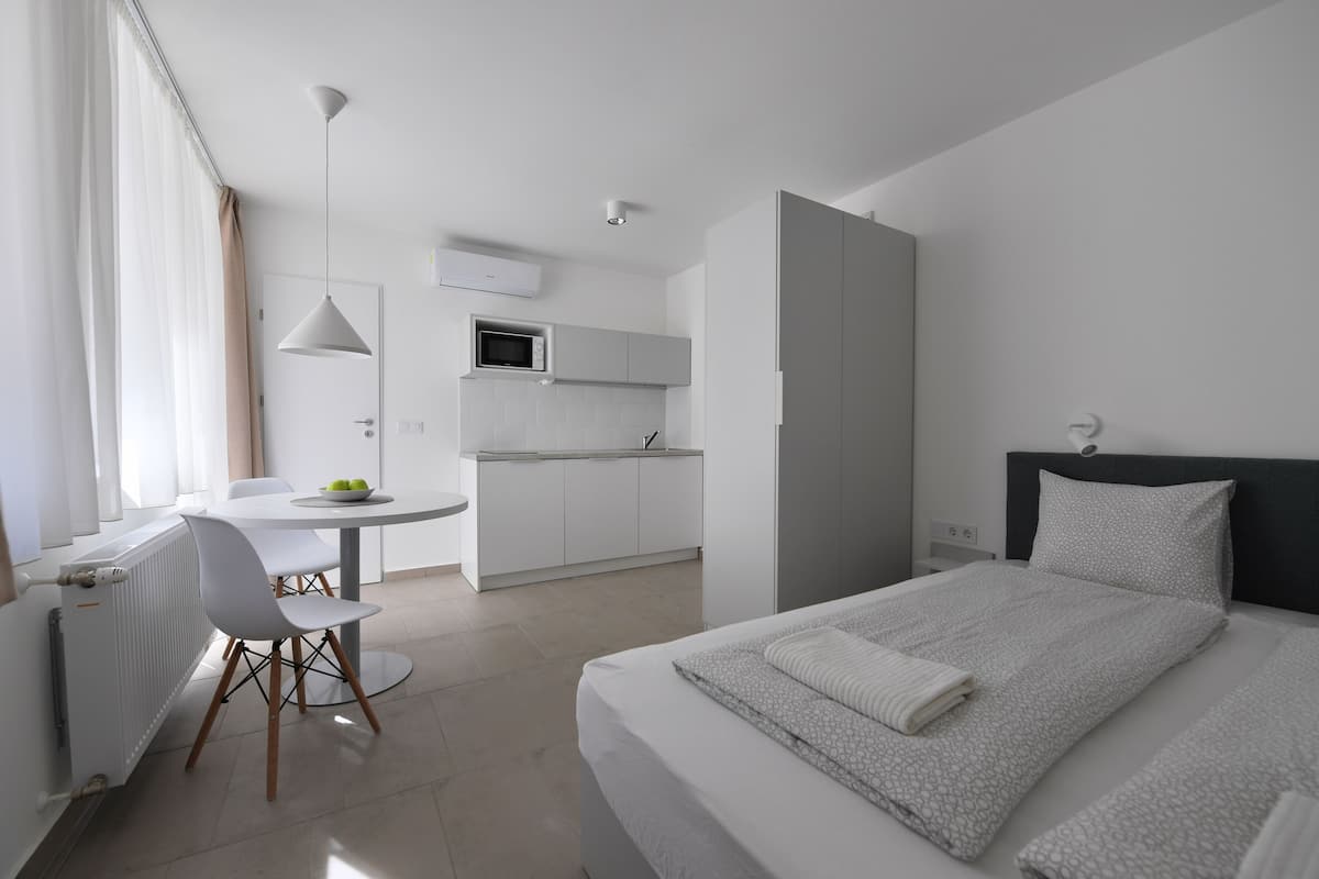 Quarto de hotel moderno com cama, escrivaninha e cozinha compacta.