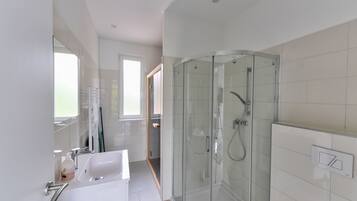 A modern bathroom with a glass-enclosed shower, a white sink, and a large mirror.