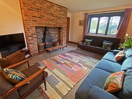 Una sala de estar acogedora con chimenea de ladrillo, televisor, sofá y un ventanal grande.