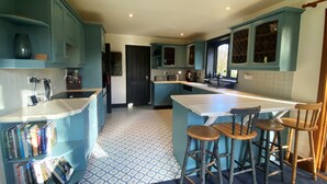 A kitchen with blue cabinets, a white countertop, and a patterned floor. There are three wooden stools and a bar area.