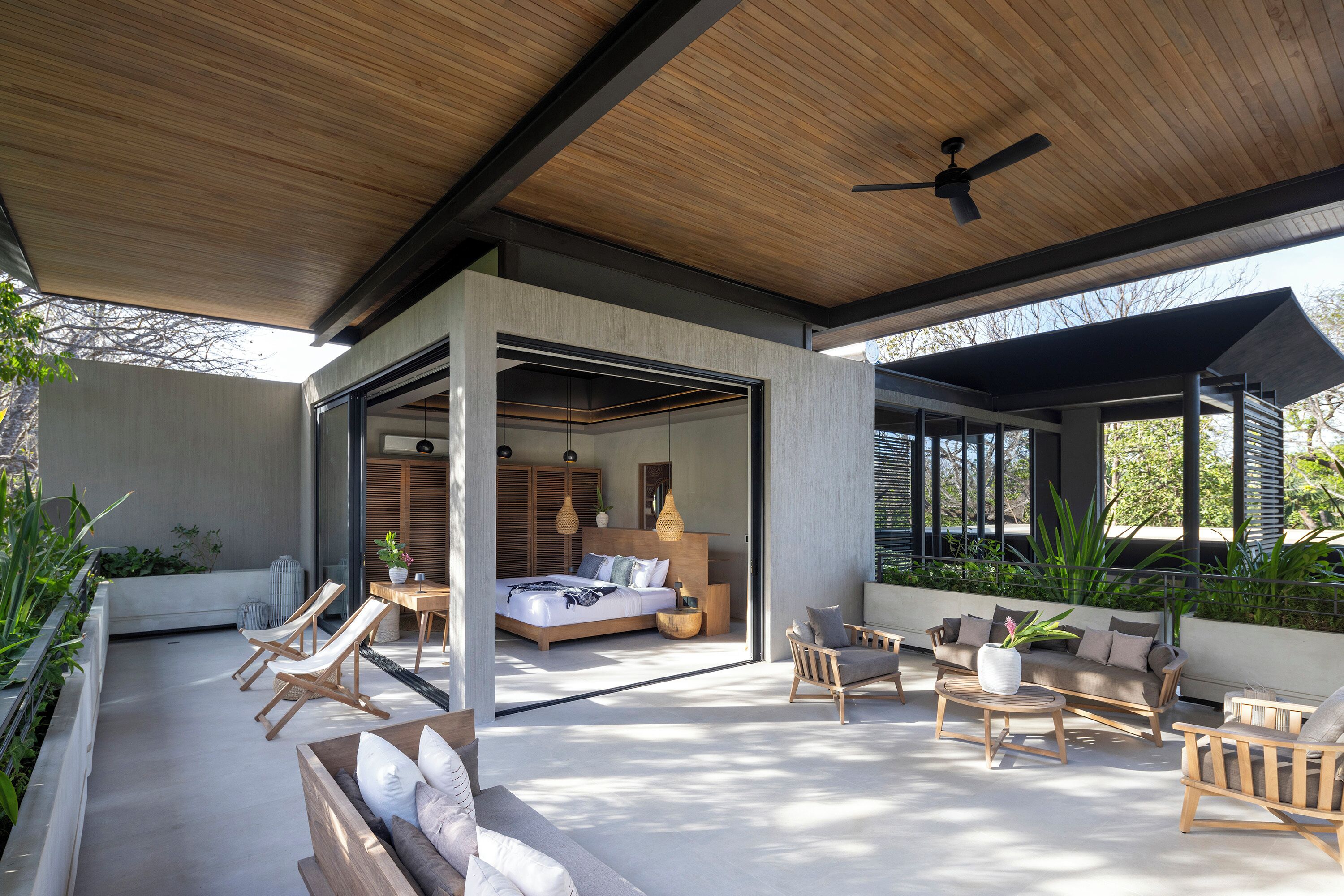 A modern outdoor living area with a bed, seating, and a ceiling fan.