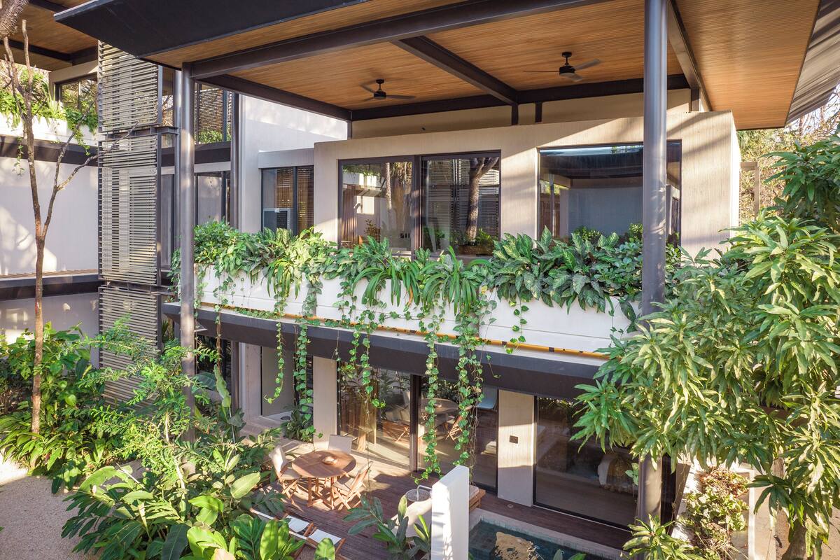 A modern house with a covered patio, large windows, and lush greenery.