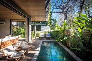 Un espace piscine extérieur moderne, doté d’une terrasse en bois avec des sièges et d’un mur en pierre.