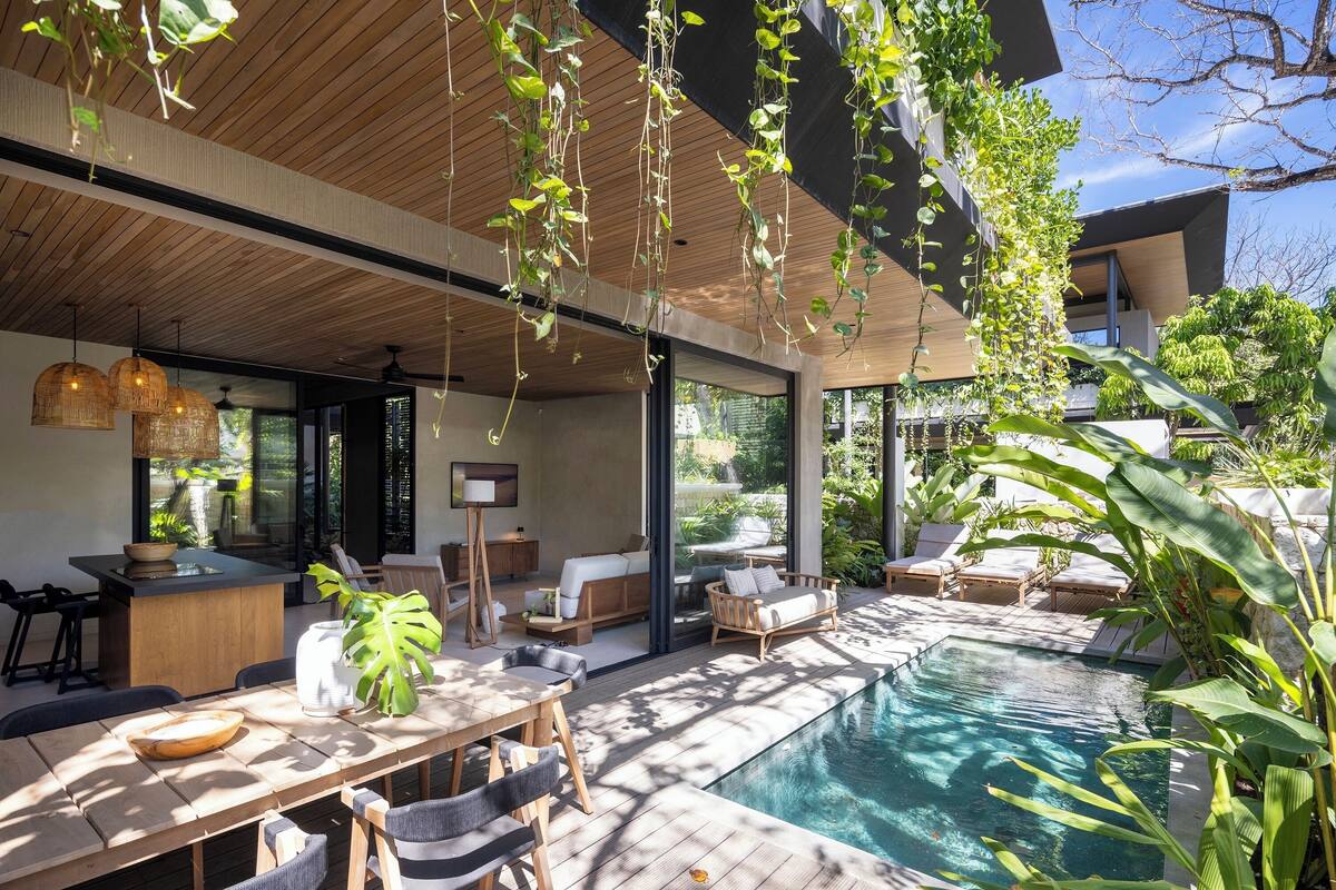 A modern outdoor pool area with wooden decking, lounge chairs, and a dining table.