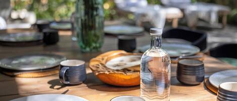 Een eettafel gedekt met borden, mokken en een fles, omringd door stoelen en een mand.