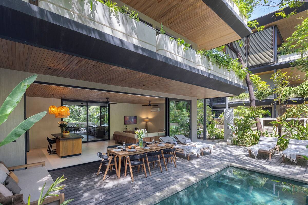 A modern outdoor living area with a pool, wooden furniture, and lush greenery.