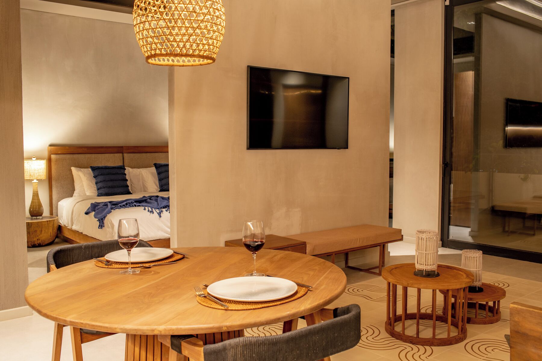 A hotel room with a wooden dining table set for two, a bench, and a large window.
