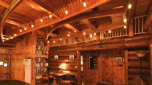 A log cabin interior with a dining area, bookshelves, and a fireplace. - Beautiful open-concept log home in quiet setting on Thompson Lake. (Otisfield)