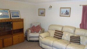 A living room with a beige leather sofa, a wooden cabinet, and two framed pictures on the wall. - Come Along and Enjoy the Beautiful Moray Coast (Buckie)